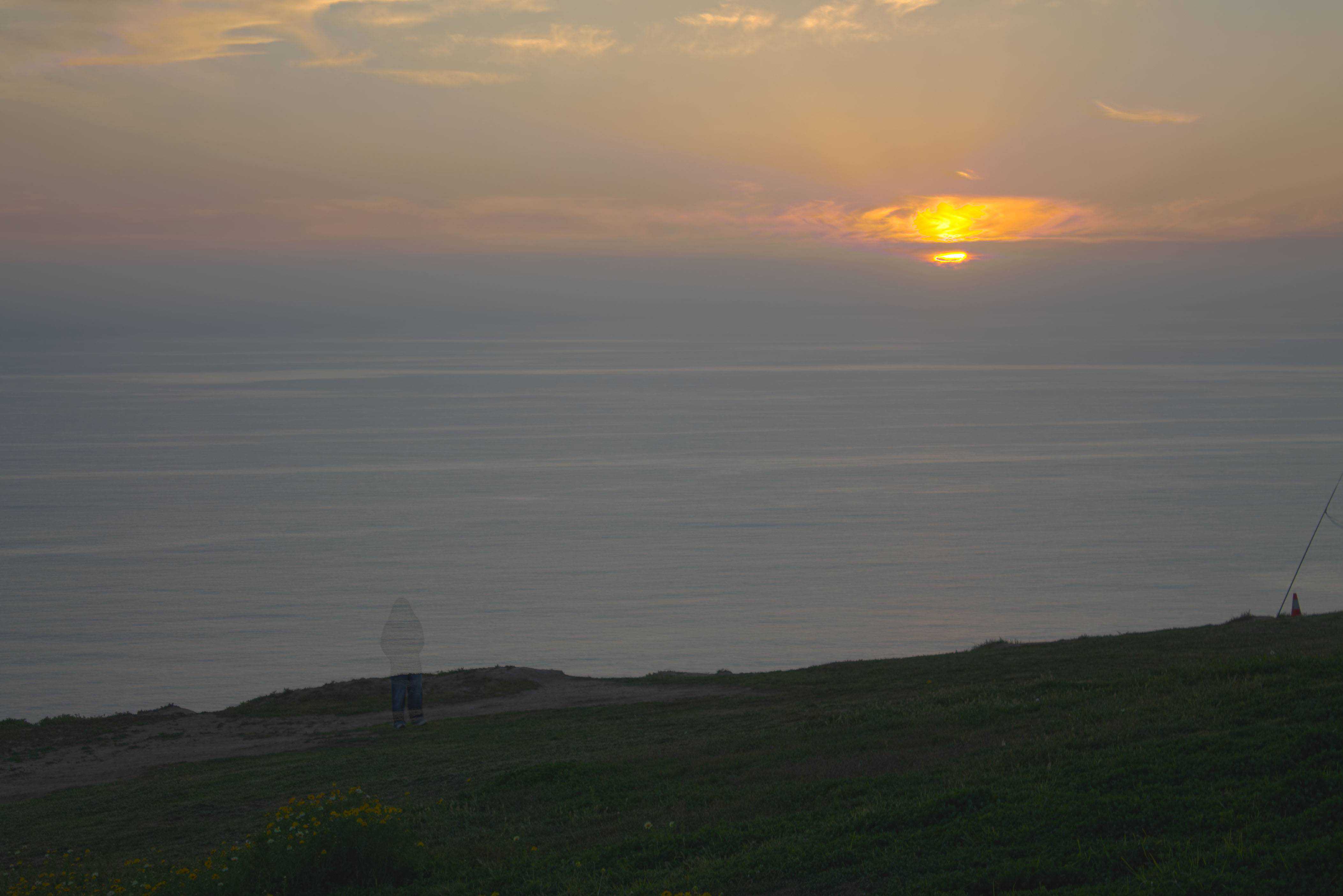 A ghostly image of a person staring out at the ocean at sunet.